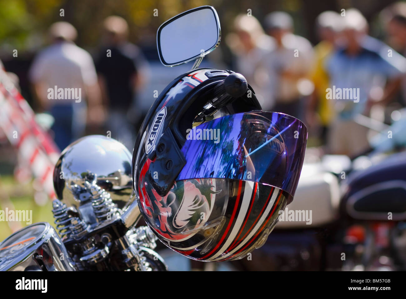 Bunte Helm drapiert auf dem Lenker eines Motorrads. Nicht erkennbare Personen im Hintergrund. Vordergrund konzentrieren. Stockfoto
