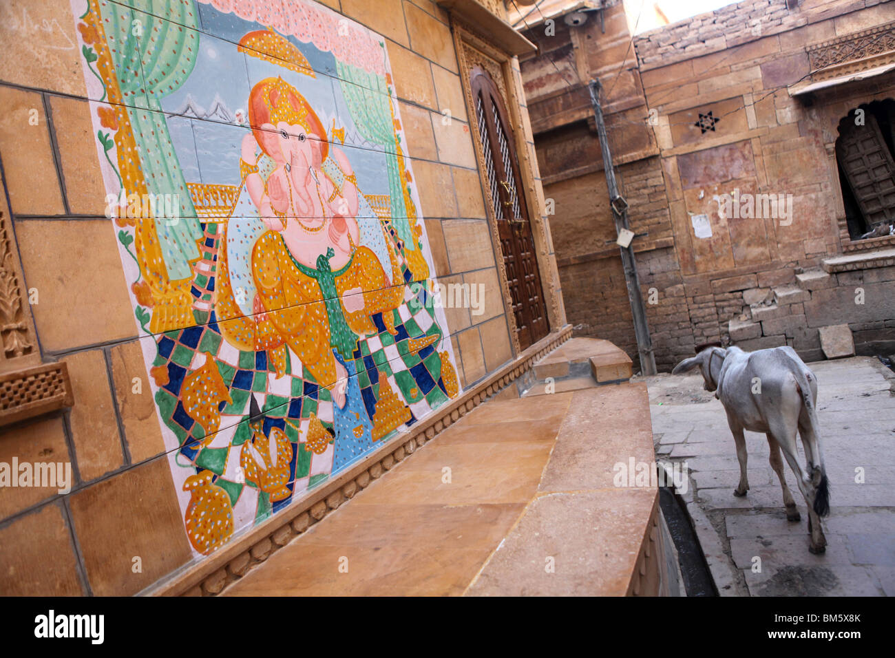 Eine Kuh wandert vorbei an einem Fresko oder Dekore von Ganesha in Jaisalmer, Rajasthan, Indien. Stockfoto