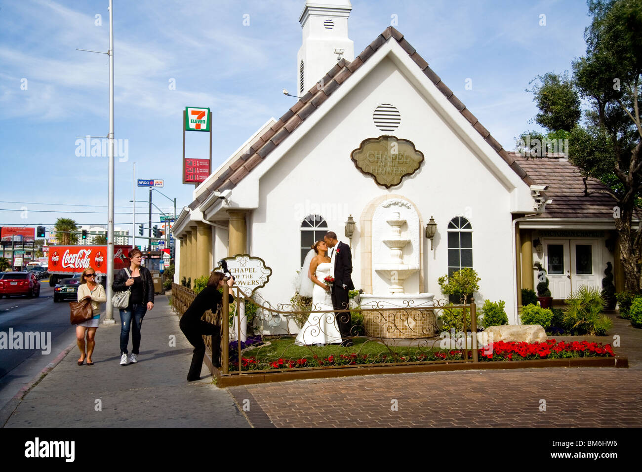 Passanten Blick tatenlos zusehen wie ein Brautpaar Kuss für Profi-Fotografen nach der Zeremonie in einer bunten Wedding Chapel. Stockfoto