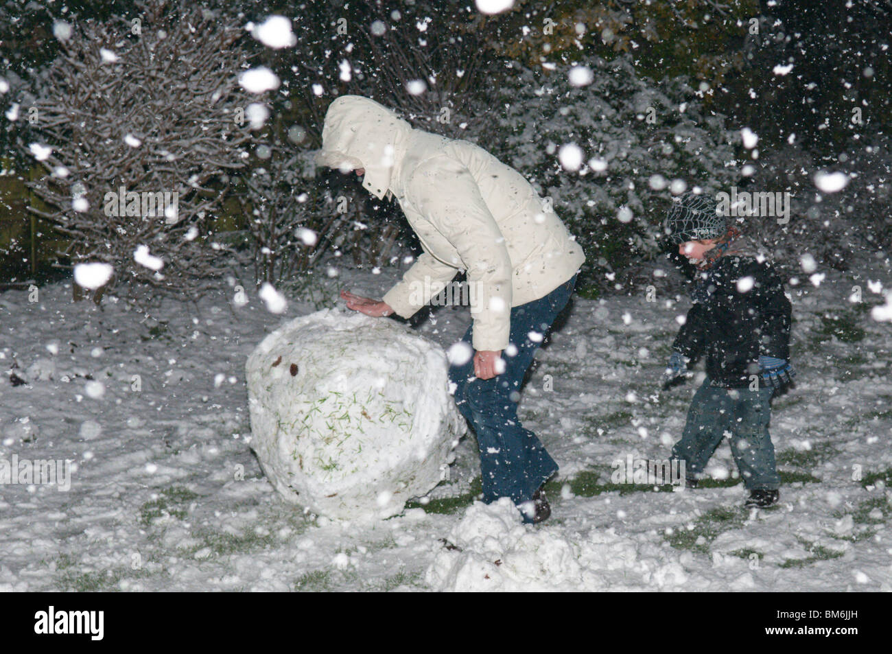 Familie Mutter Sohn in starkem Schneefall bei Nacht Gebäude Schneemann im Garten in der Nacht Stockfoto
