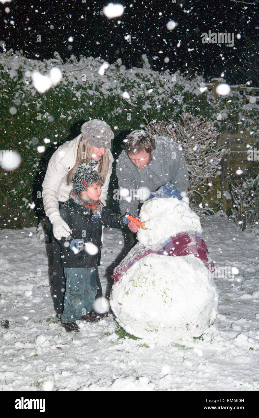 Familie Mutter Vater Sohn in starkem Schneefall bei Nacht Gebäude Schneemann im Garten in der Nacht Stockfoto