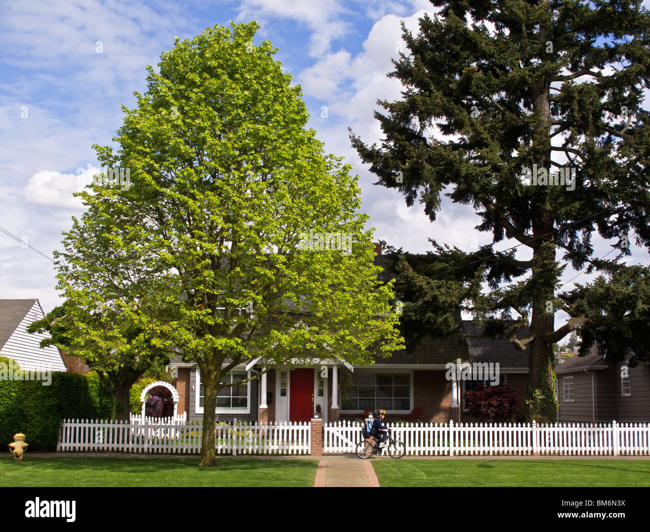 Junge mit dem Fahrrad fährt vorbei an Haus mit weißen Lattenzaun im Frühjahr, Magnolia Nachbarschaft, Seattle, Washington Stockfoto