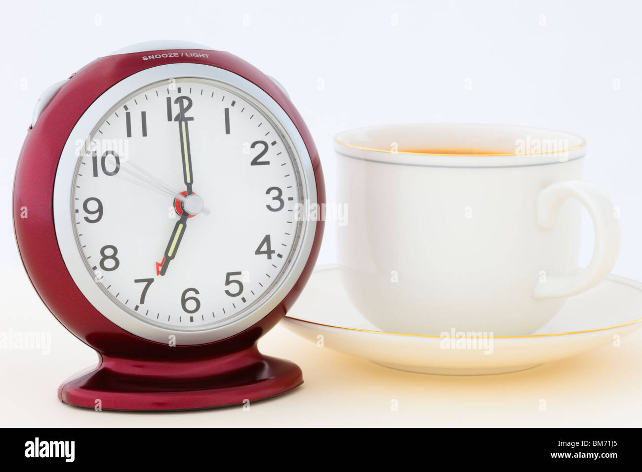 Kaffee Tasse und Untertasse mit einem roten Wecker um 7 Uhr in der Früh nur Sekunden, bevor der Wecker klingelt. Aufwachen und Kaffee im Bett Konzept. England Großbritannien Großbritannien Stockfoto