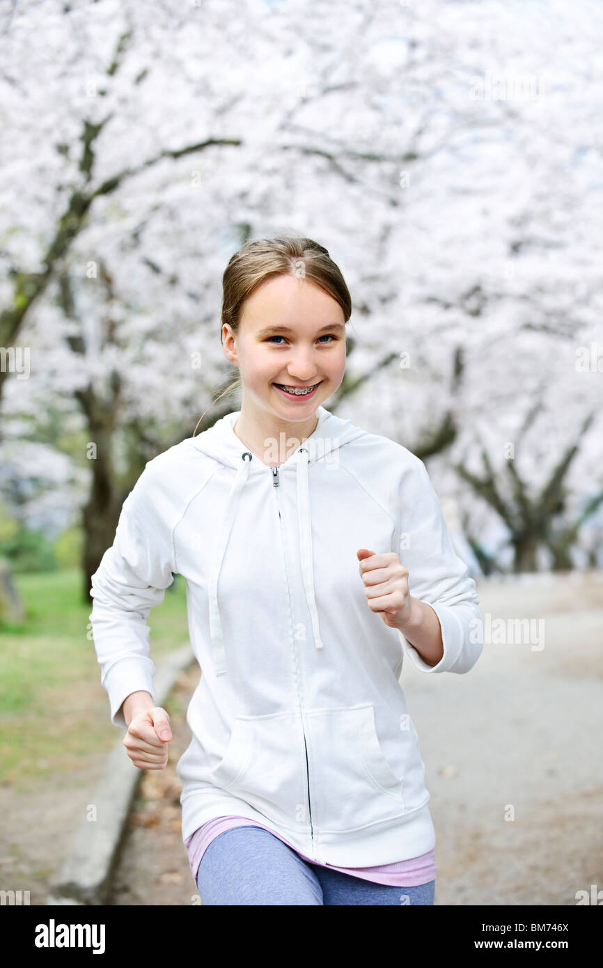 Schöne Teenager-Mädchen Joggen im Park mit blühenden Apfelbäumen Stockfoto