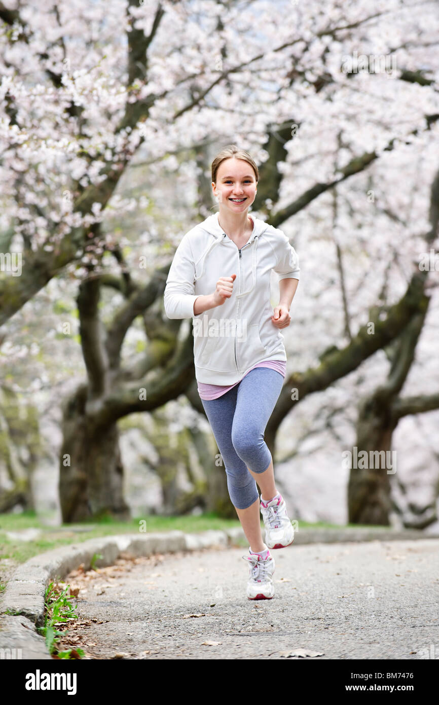 Schöne Teenager-Mädchen Joggen im Park mit blühenden Apfelbäumen Stockfoto