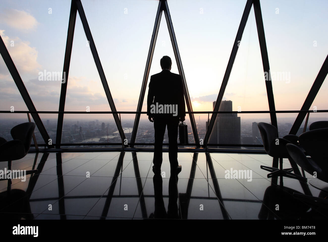 Ein Geschäftsmann Stand mit seiner Aktentasche am oberen Rand der Wolkenkratzer Gherkin in der City of London, U.K Stockfoto