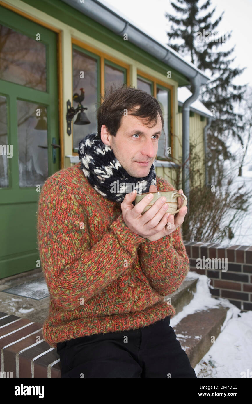 Ein Mann sitzt auf der vorderen Stoop eines Hauses mit einem heißen Getränk Stockfoto