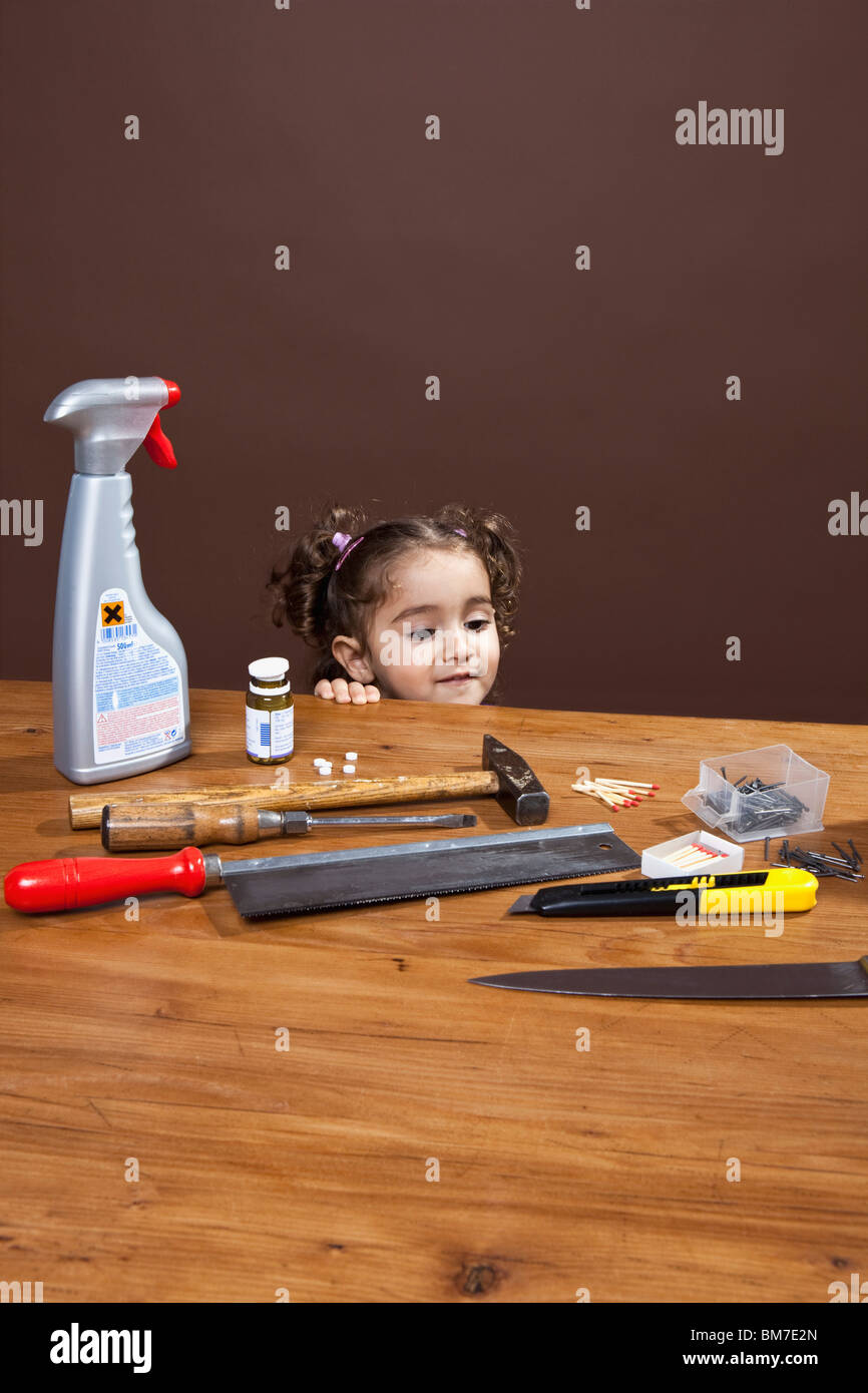 Ein junges Mädchen Blick auf gefährliche Gegenstände auf einem Tisch, Studio gedreht Stockfoto