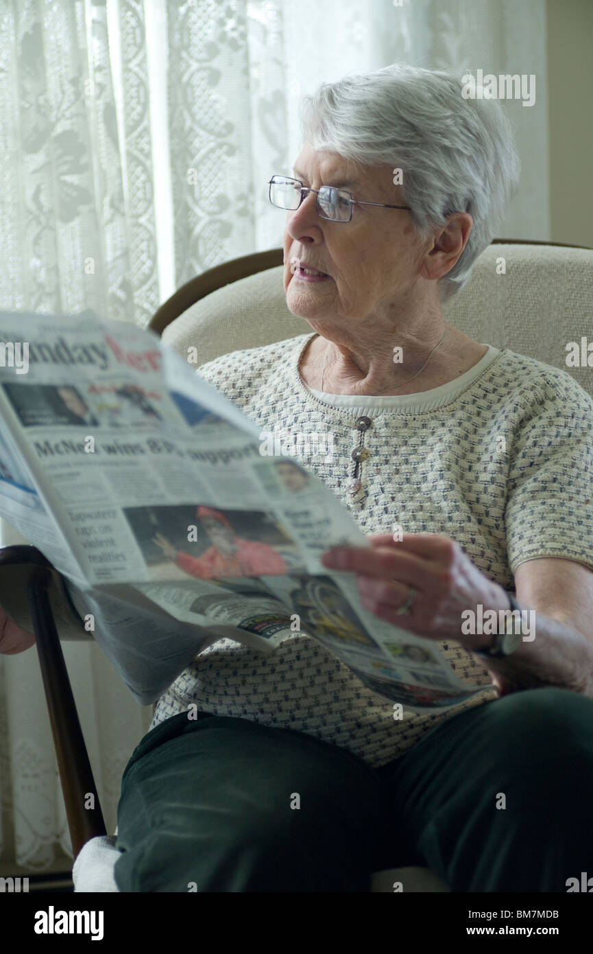 Alte Frau sitzt im Stuhl und Las Zeitung. Stockfoto