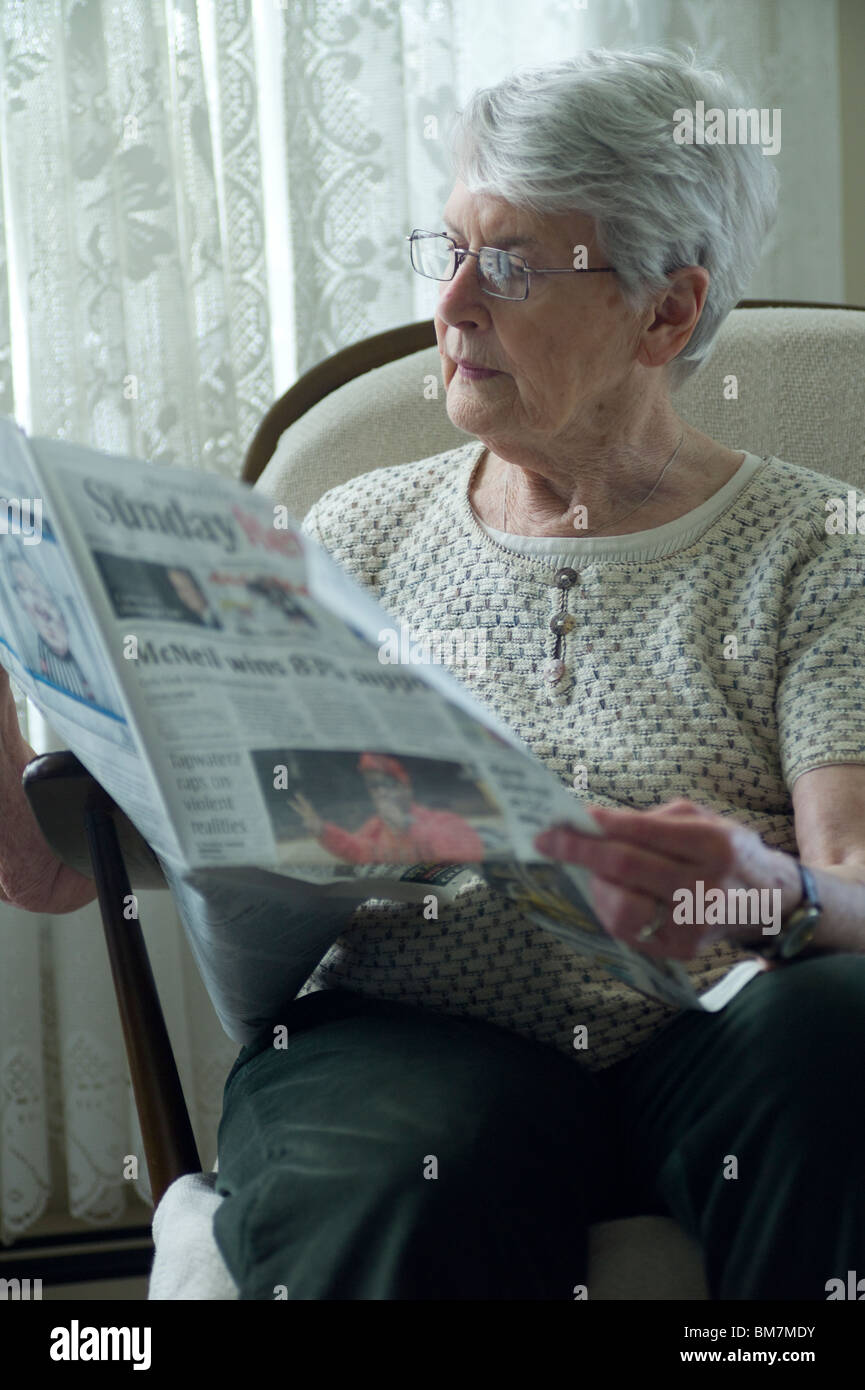 Alte Frau sitzt im Stuhl und Las Zeitung. Stockfoto