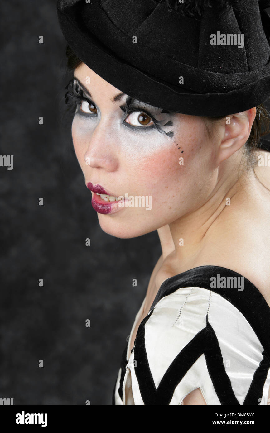 Junge Frau in schwarz / weiß gekleidet, Clown-Outfit und schwarzen Hut mit Feder Wimpern Stockfoto