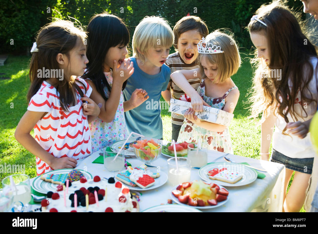 Mädchen Geschenk auf Geburtstagsparty zu öffnen, wie Freunde beobachten Stockfoto