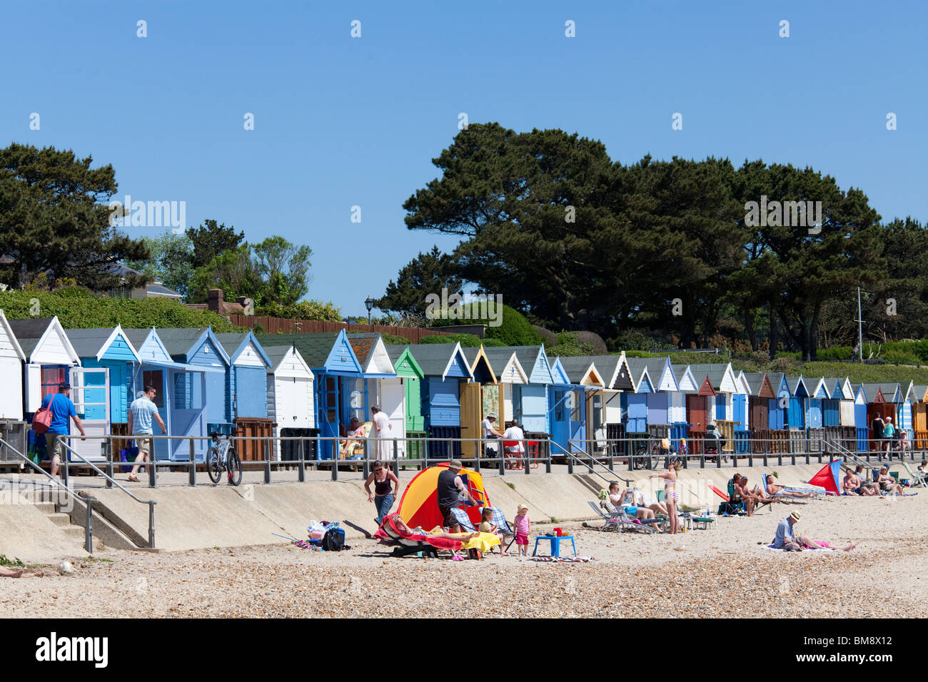 Reihe von bunten Strandhäuschen und Urlauber an der Küste von Mudeford. Stockfoto