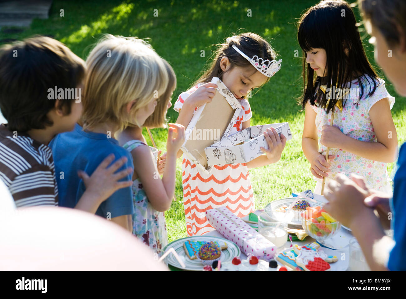 Mädchen Geschenk auf Geburtstagsparty zu öffnen, wie Freunde beobachten Stockfoto