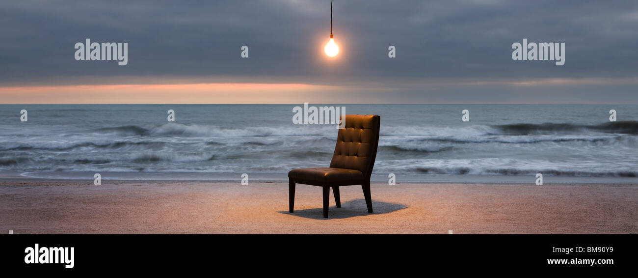 Glühbirne leuchtet über Stuhl am Strand bei Sonnenuntergang Stockfoto