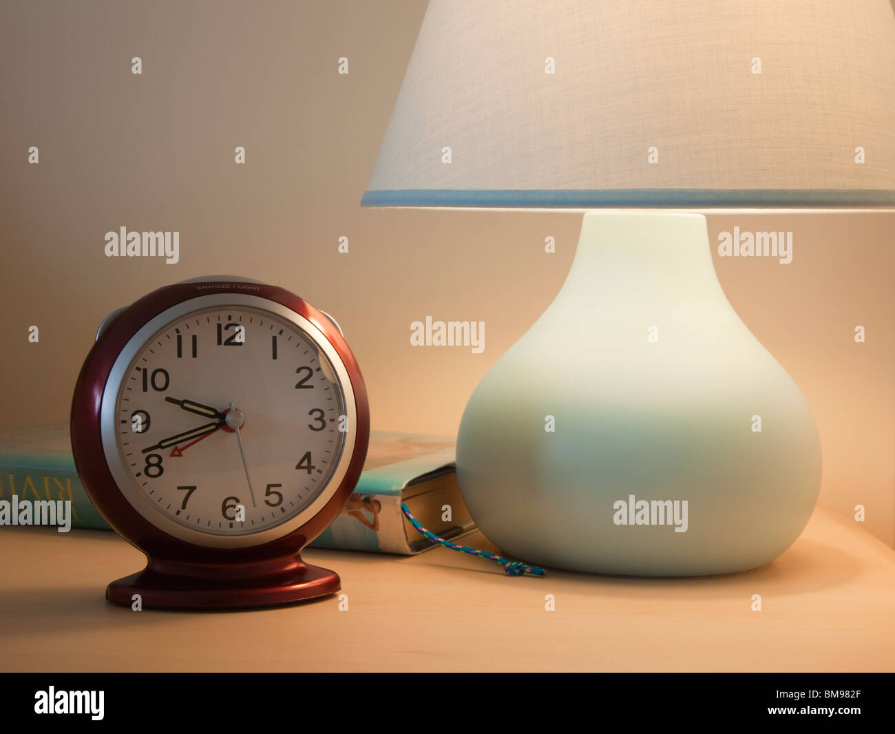 Nahaufnahme von einem Wecker mit beleuchteten Nachttisch Lampe und buchen Sie vor dem Schlafengehen am Abend. England Großbritannien Großbritannien Stockfoto