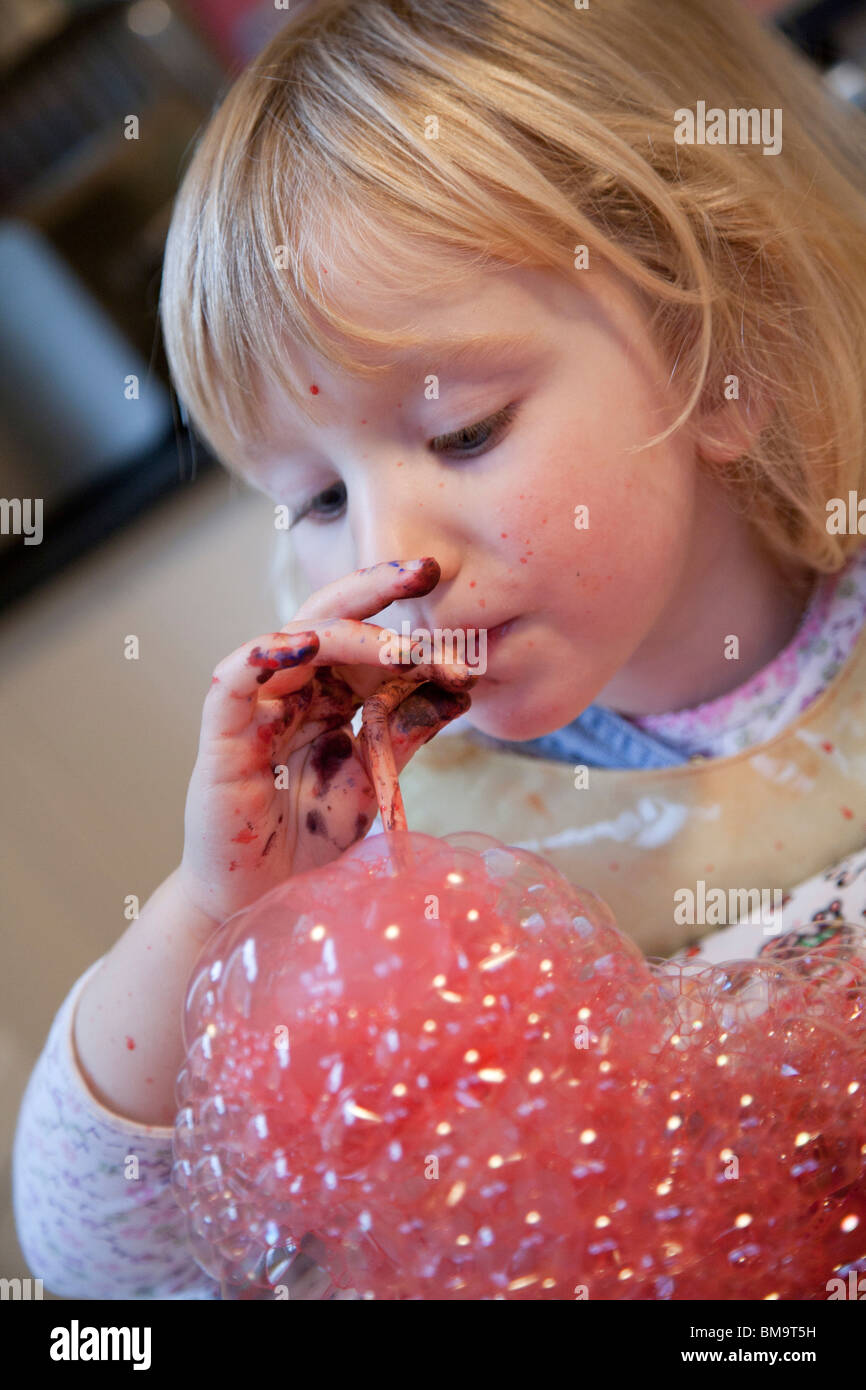 3-jähriges Mädchen bläst Seifenblasen in Farbe in die Küche zu Hause Stockfoto
