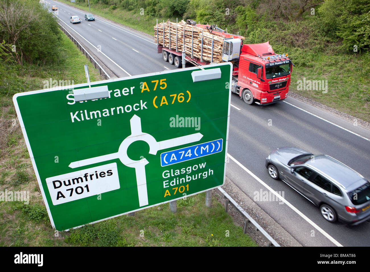 Straßenschild und Wegbeschreibungen am Kreisverkehr auf der A75 in der Nähe von Dumfries mit PKW und LKW vorbei UK zu beschleunigen Stockfoto