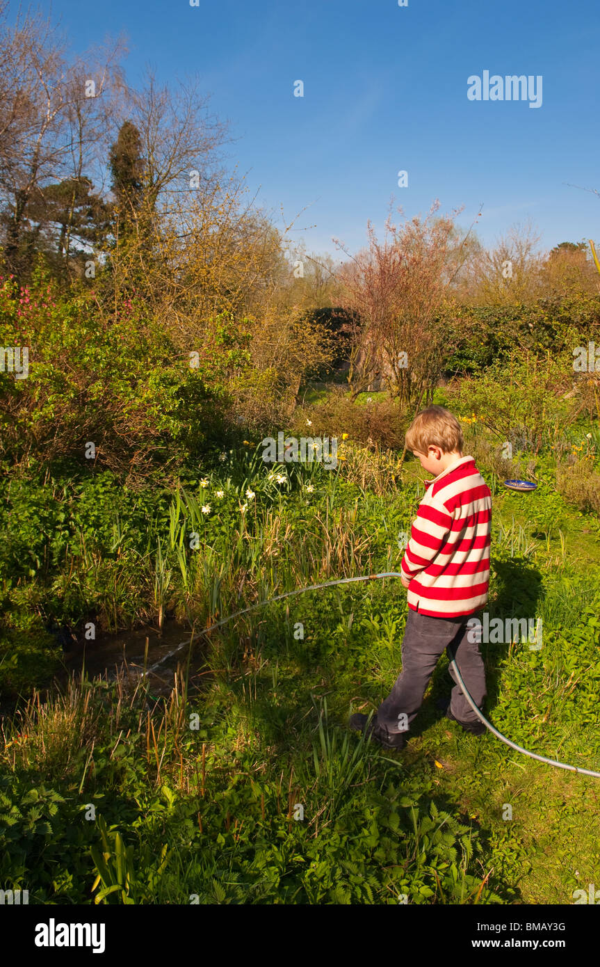Ein MODEL Release Bild eines 6-jährigen Jungen füllen einen Teich mit einem Schlauch Gartenschlauch in England, Großbritannien, Vereinigtes Königreich Stockfoto