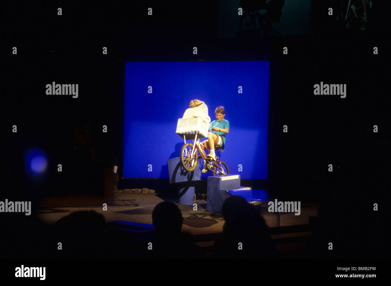 Jungen Fahrrad mit E.T. im Korb vor blue Screen kombiniert, um ihn auf TV-Monitor für Publikum fliegen scheinen zu machen Stockfoto