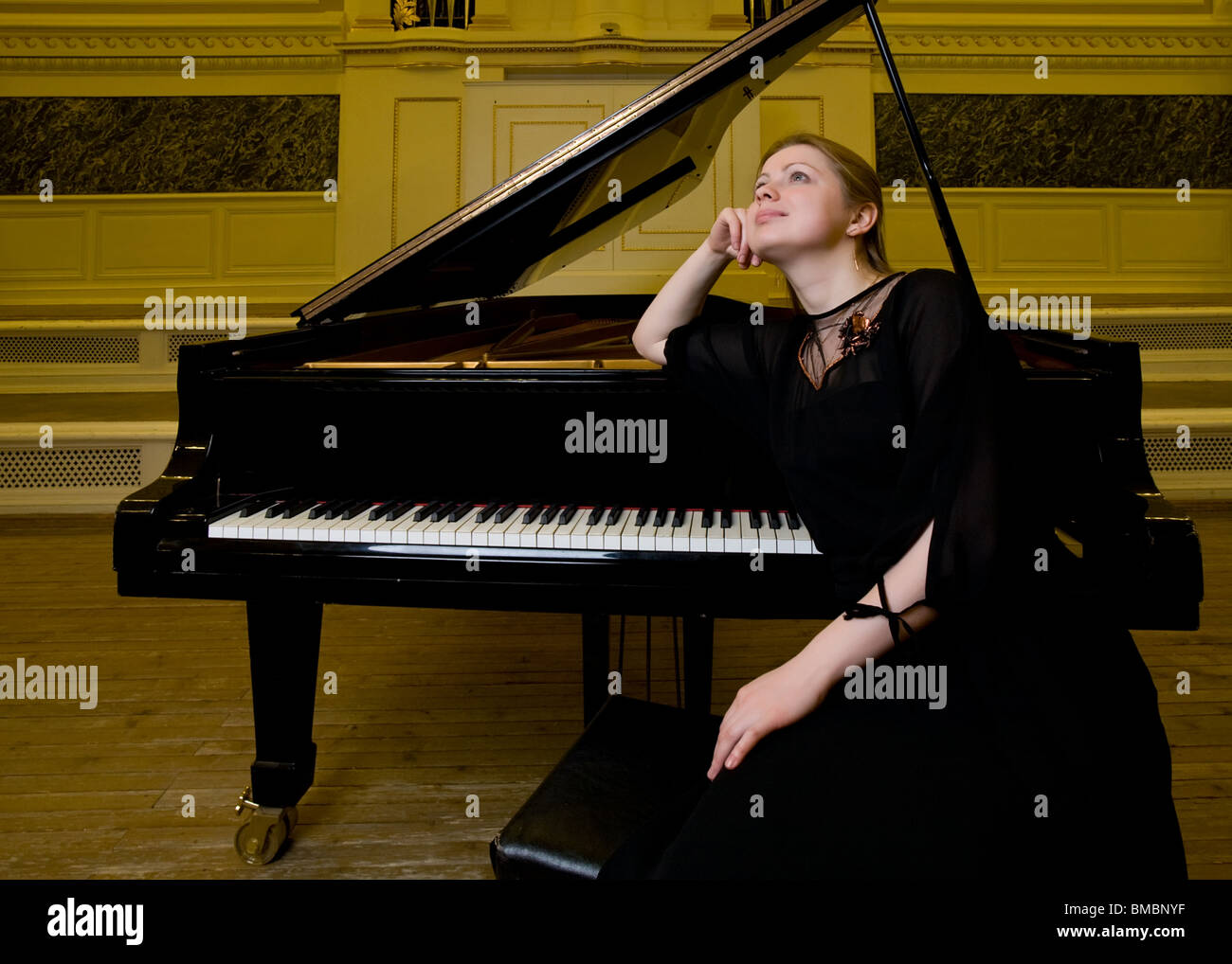 Girl in schwarzer Kleidung sitzt in der Nähe eines Klaviers und verträumt schaut Stockfoto