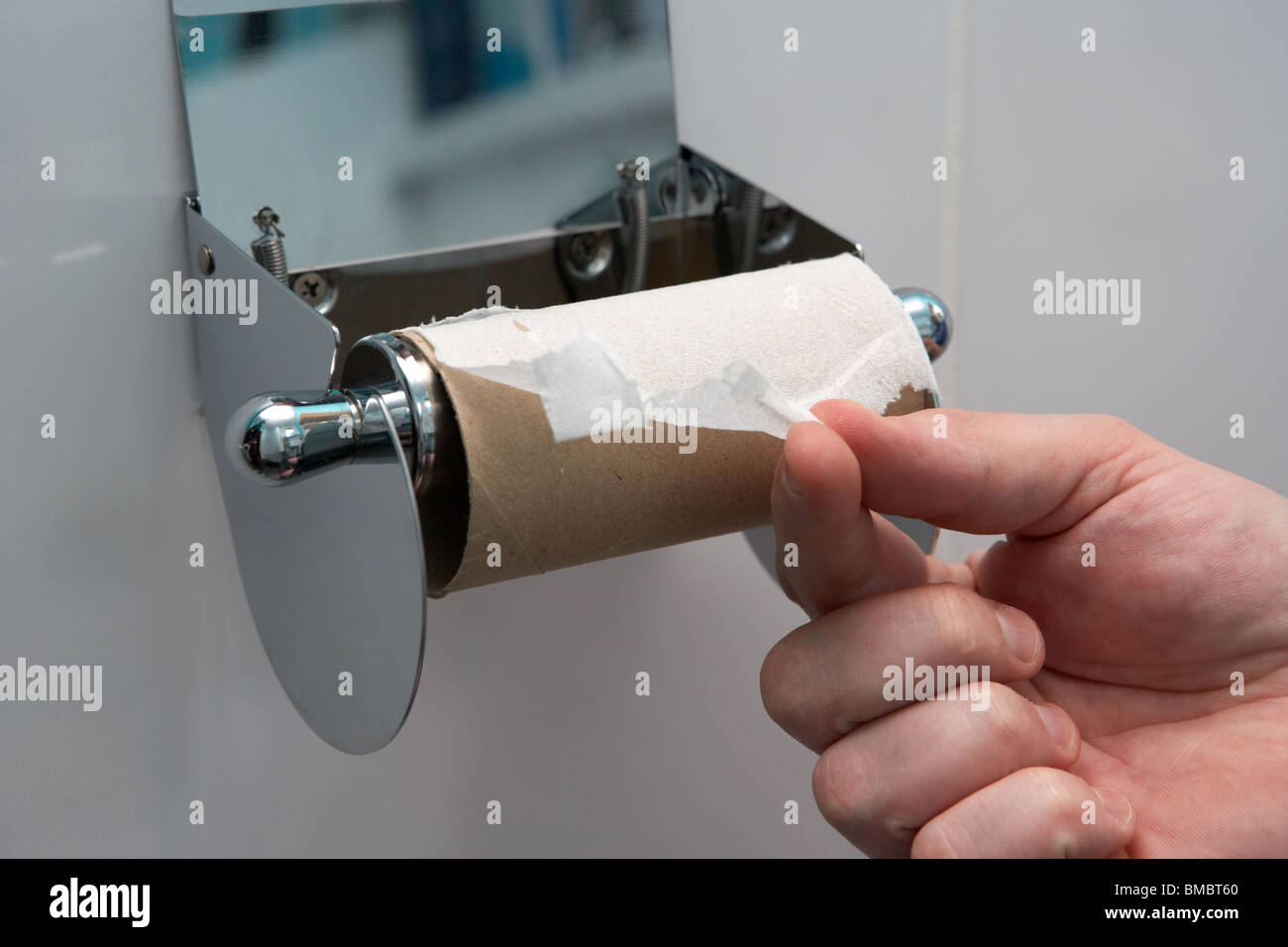 Die Hand von Mans zieht das letzte noch vorhandene Blatt toilettenpapier auf einem toilettenrollenhalter aus der Rollenkrise des Klo Stockfoto
