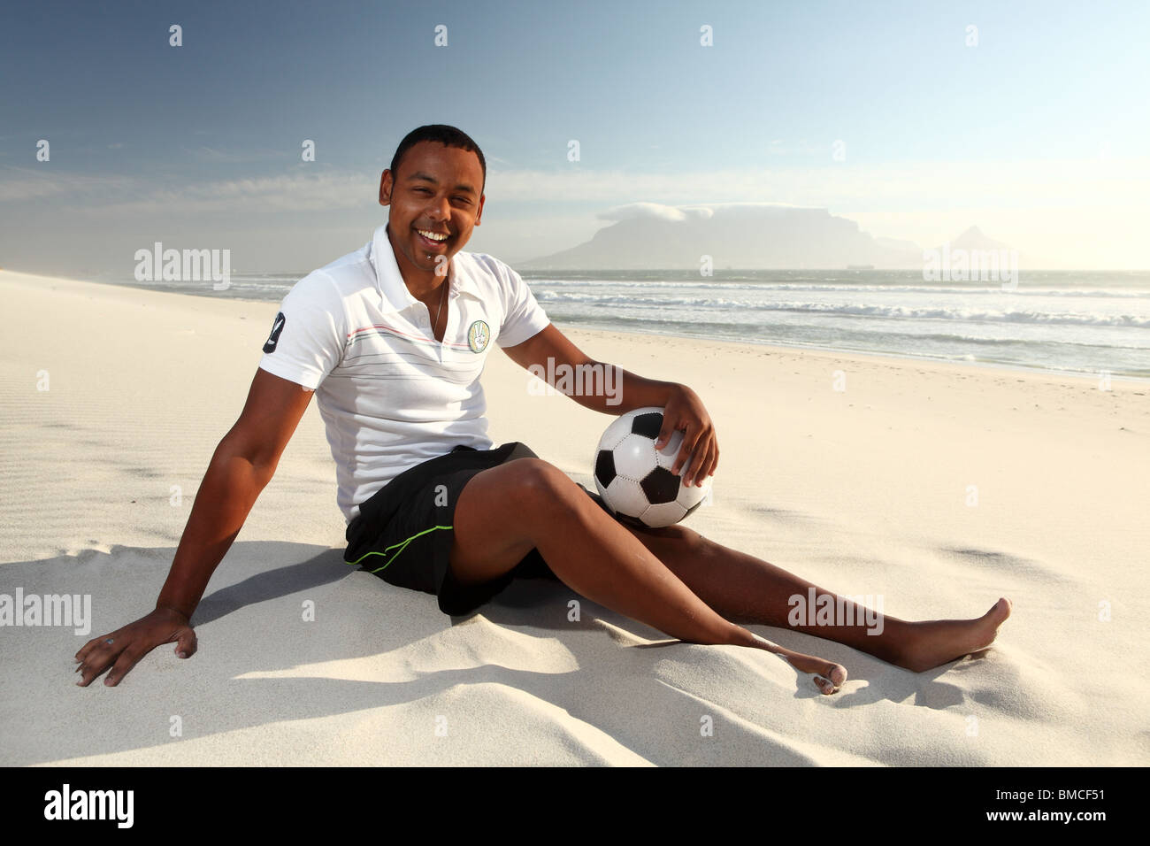 Ein junger Mann mit einem Fußball am Strand von Blouberg Strand in Kapstadt, Südafrika Stockfoto