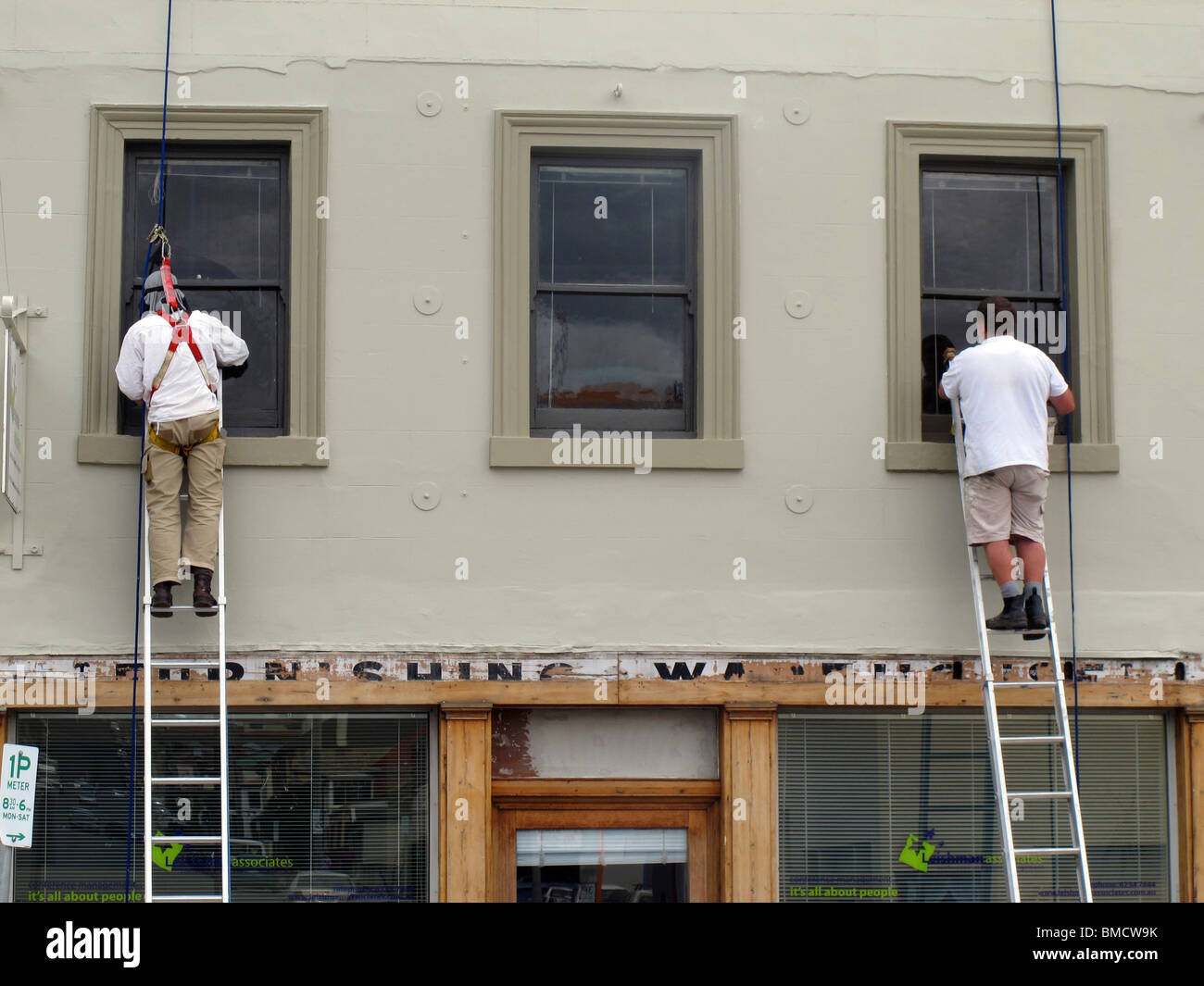 Zwei Maler auf Leitern, die die Fensterrahmen eines historischen Ladenlagers in der Melville Street, Hobart, Tasmanien, bemalen. Einer trägt einen Auffanggurt. Stockfoto