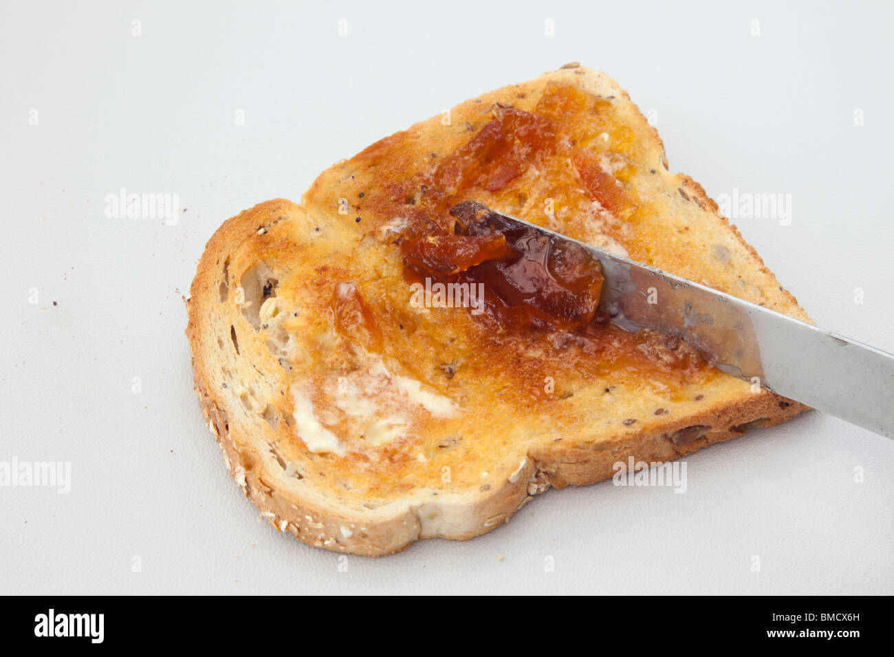 Marmelade auf eine Scheibe Toast mit zerlassener Butter mit einem Messer zu verbreiten Stockfoto