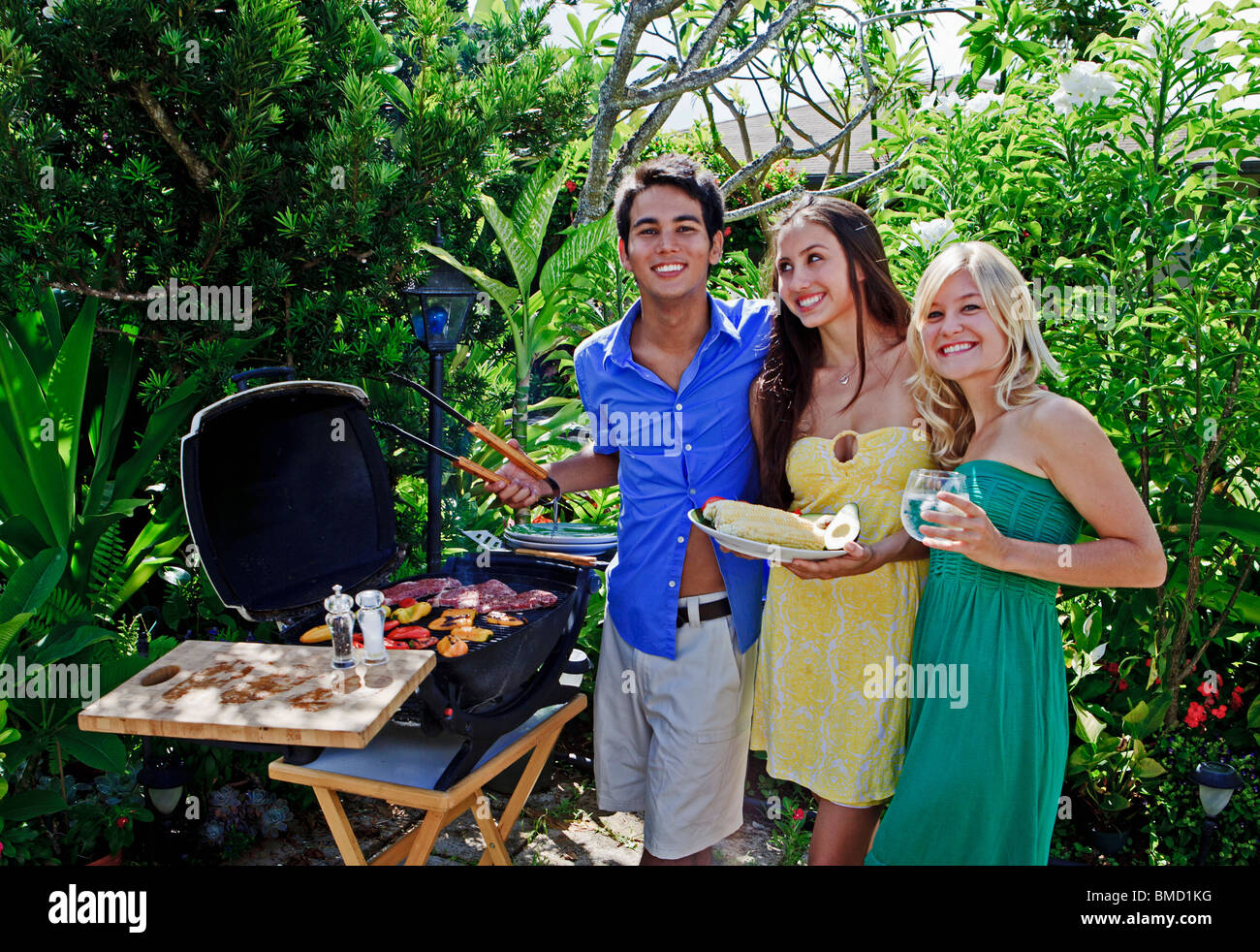 drei Freunde, die eine Mittagessen vom Grill im tropischen Garten Stockfoto