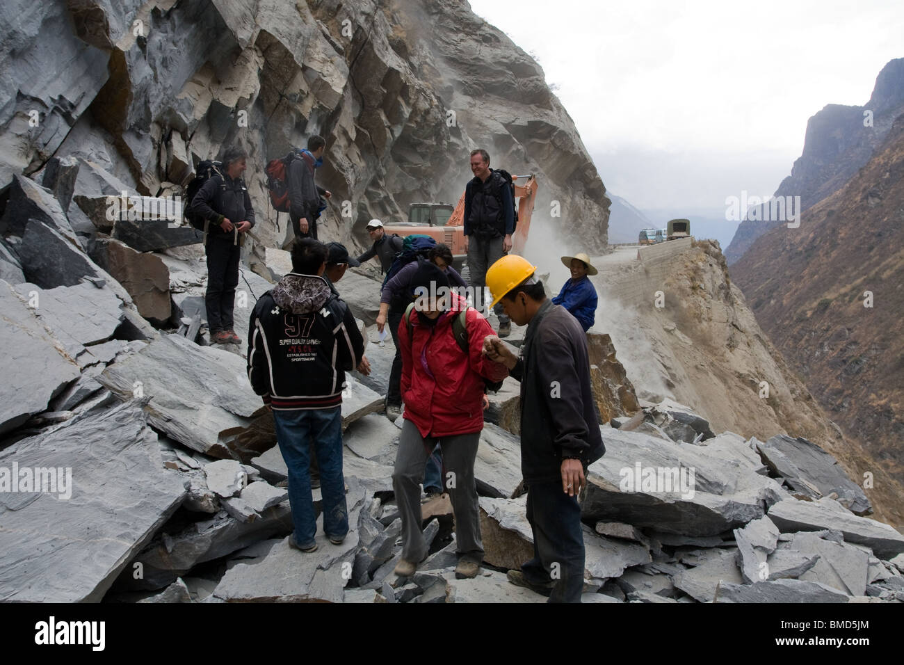Chinesische Arbeiter helfen Touristen Wanderer einen Haufen von Felsen in einer Yangzi Damm Baustelle in der Nähe von Trek Tigersprung-Schlucht zu überqueren. Stockfoto