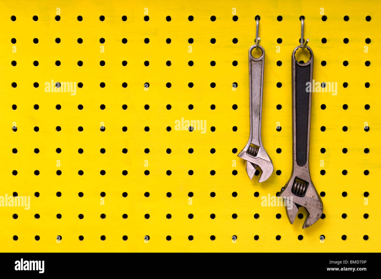 Paar Metall Schraubenschlüssel hängen zusammen aus Haken auf gelben Pegboard. Stockfoto