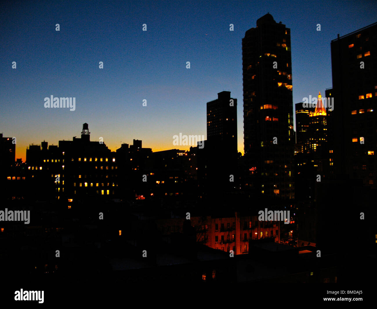 Teil der Lower Manhattan Skyline, bei Sonnenuntergang gesehen. Silhouetten von hohen, beleuchteten Gebäuden gegen einen blauen und orangefarbenen Himmel. Stockfoto