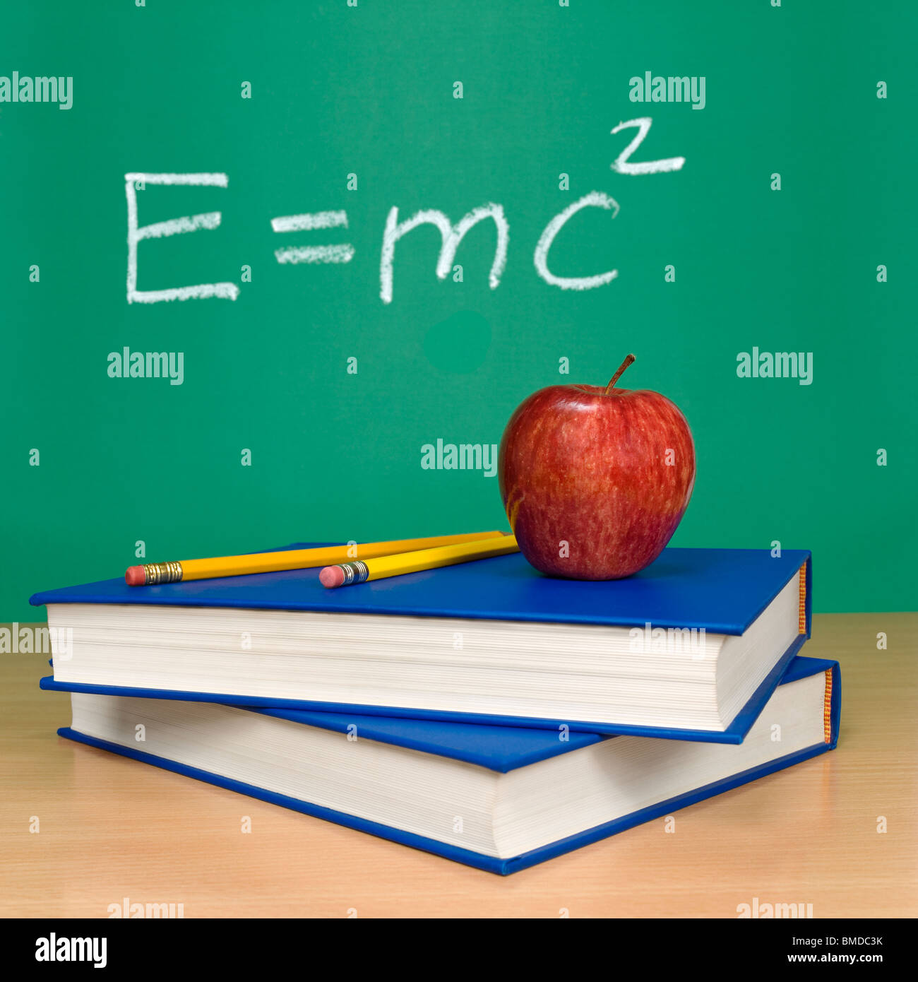 Einsteins Formel der Relativitätstheorie auf einer Kreidetafel. Bücher, Stifte und einen Apfel im Vordergrund. Stockfoto