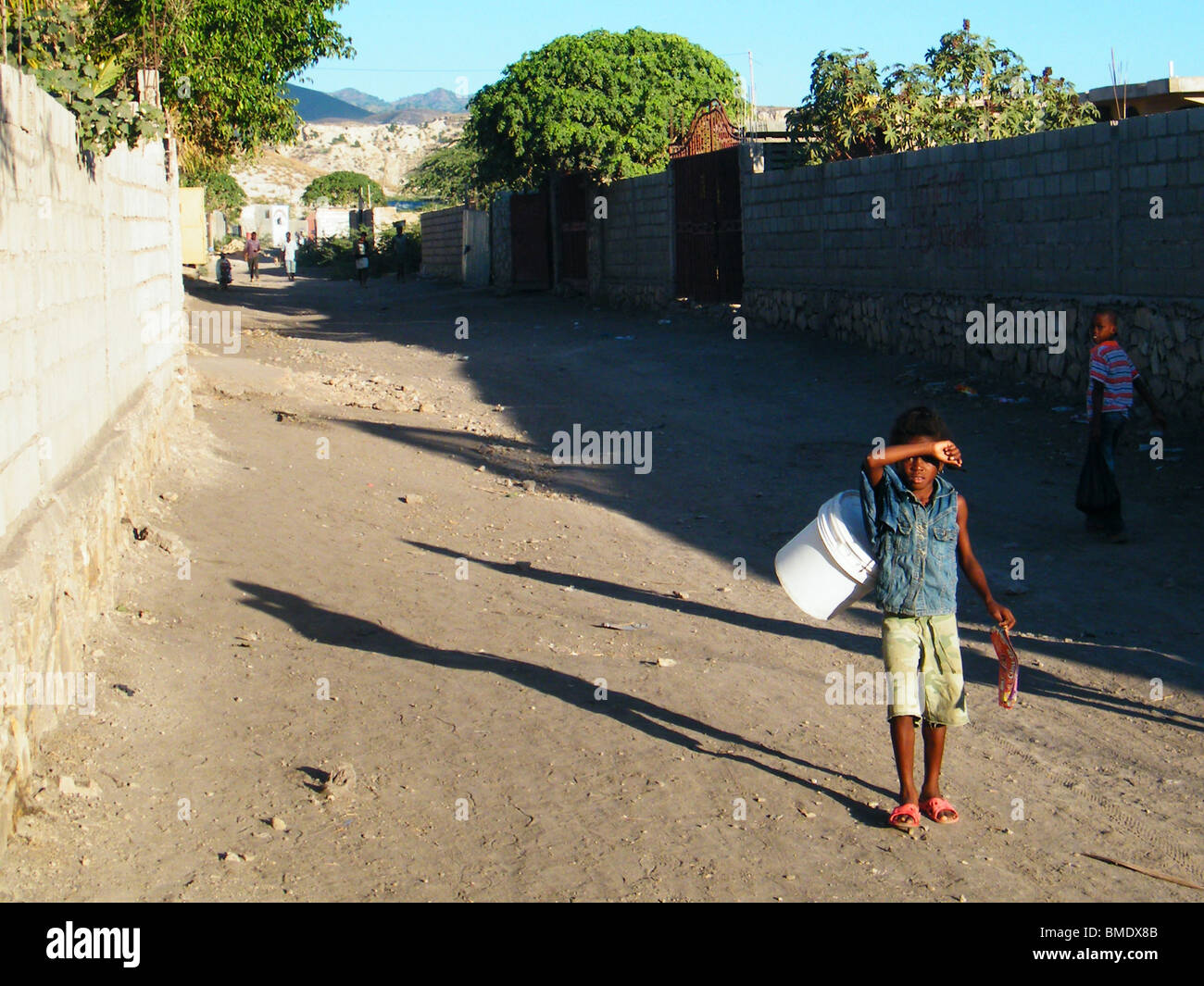 Ein junges Mädchen, geschickt, um Wasser zu sammeln geht auf einer staubigen Straße in Gonaives, Haiti Stockfoto