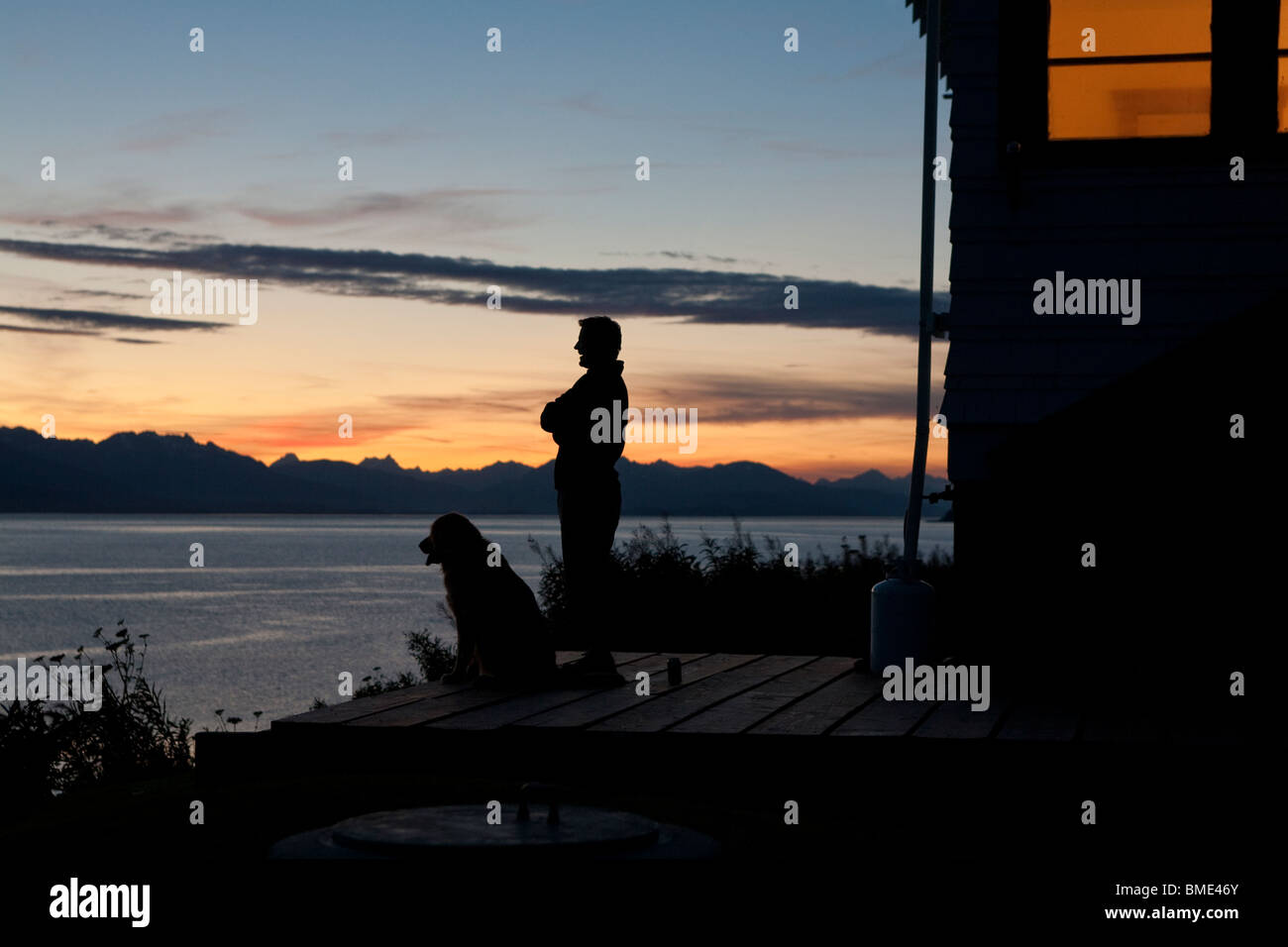 Mensch und Hund bewundern den Sonnenuntergang Sonnenuntergang über der Chatham-Straße von der Hüter-Hütte auf den Punkt Retreat Leuchtturm, Alaska Stockfoto