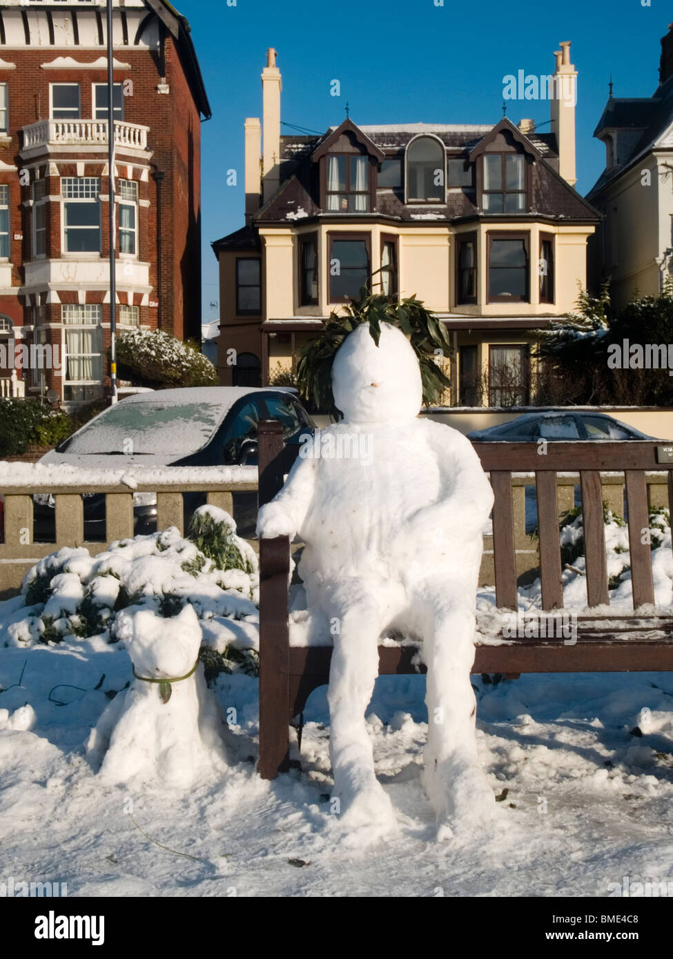 Schneemann mit seinem Schnee Hund neben ihm sitzen auf einer Bank sitzend Stockfoto