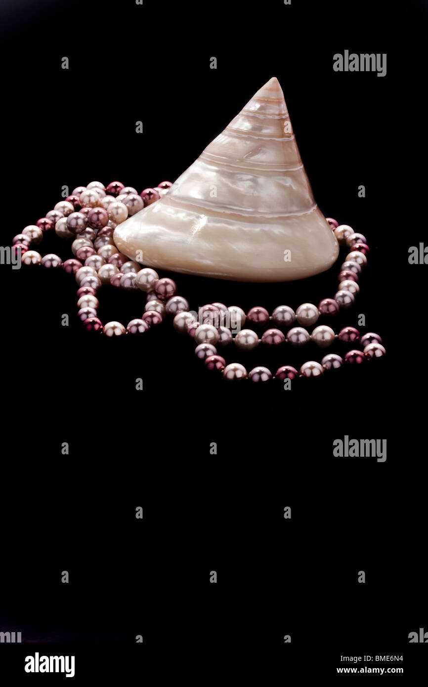 Spiral Shell mit Pfirsich und weißen farbigen Perlen dekorativ drapiert über und um auf einem schwarzen Hintergrund und Oberfläche Stockfoto