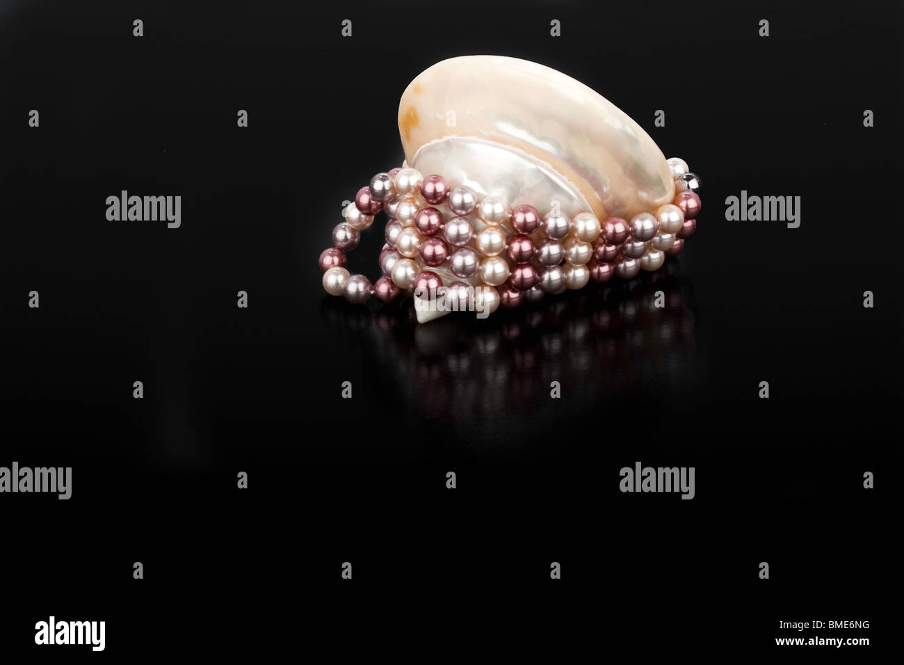 Spiral Shell mit Pfirsich und weißen farbigen Perlen dekorativ drapiert über und um auf einem schwarzen Hintergrund und Oberfläche Stockfoto