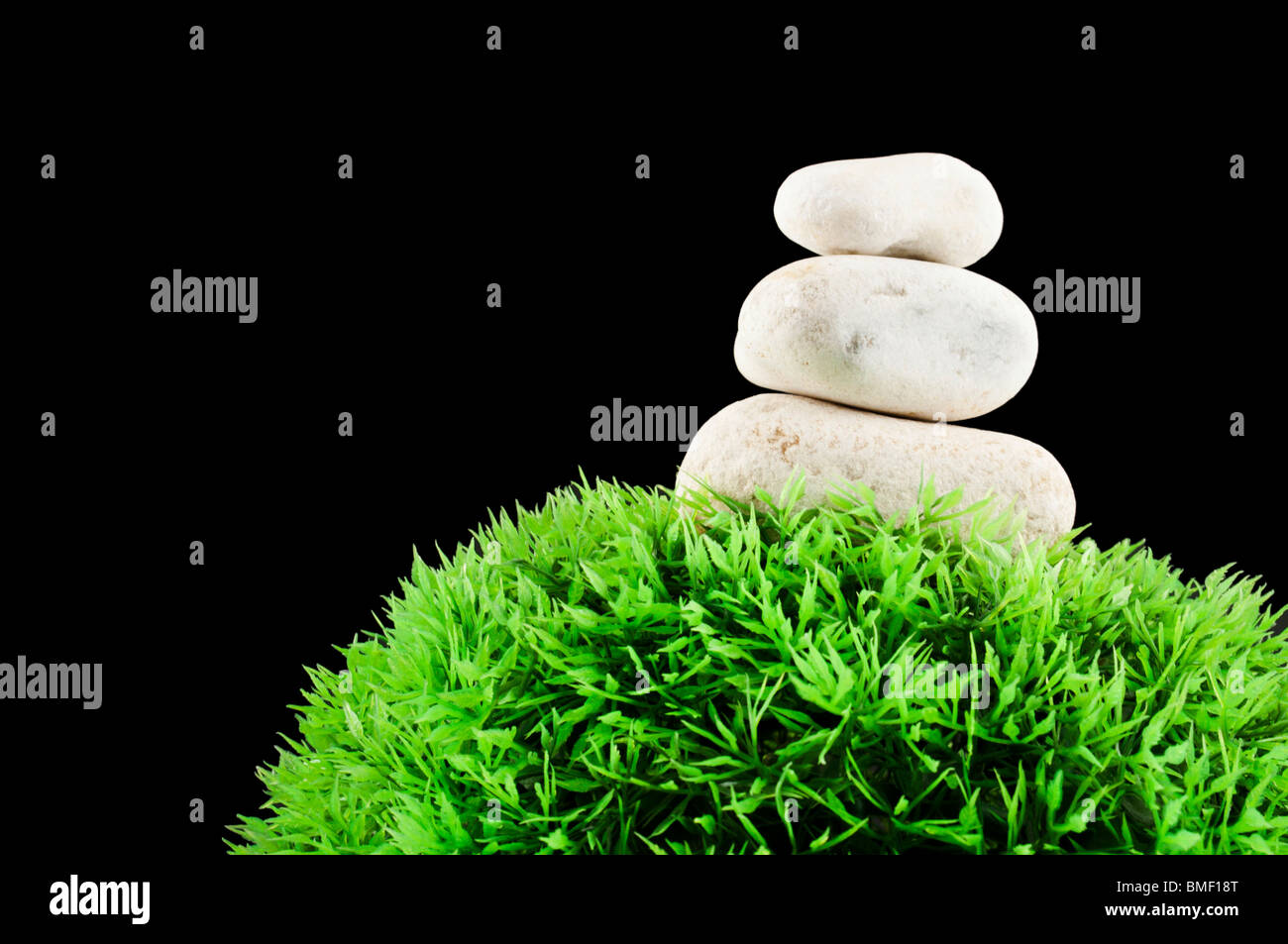 Drei Steinen über eine Rasen-Kunststoff-Kugel, isoliert auf schwarz Stockfoto