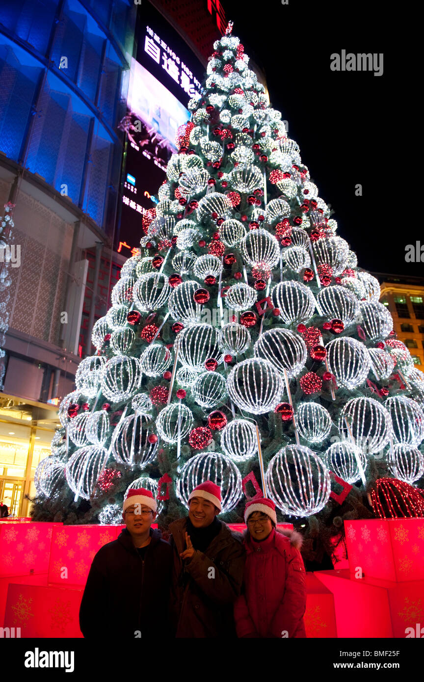 Menschen posieren für Fotos vor einem schön beleuchteten Weihnachtsbaum am Heiligabend, Peking, China Stockfoto