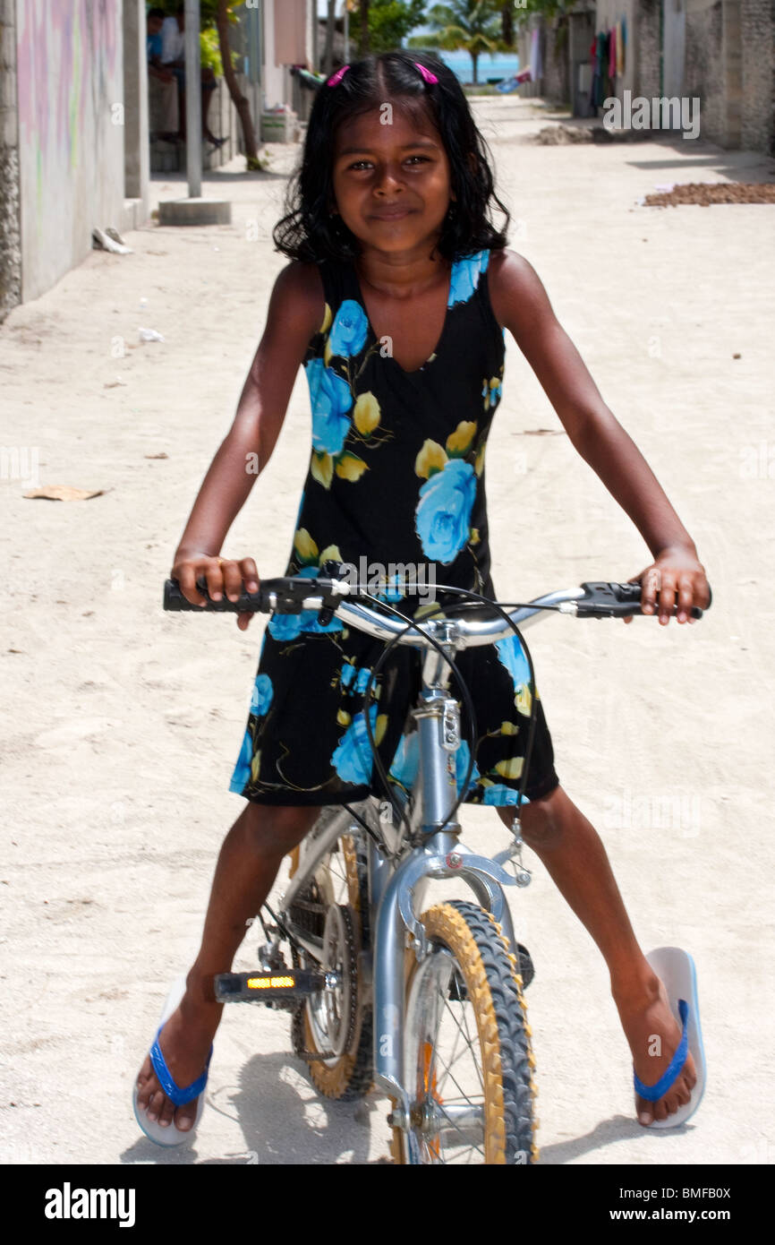 Maledivische junge Mädchen lächelnd in die Kamera sitzt auf einem modernen Fahrrad auf einer Sandinsel Straße schaut. Stockfoto