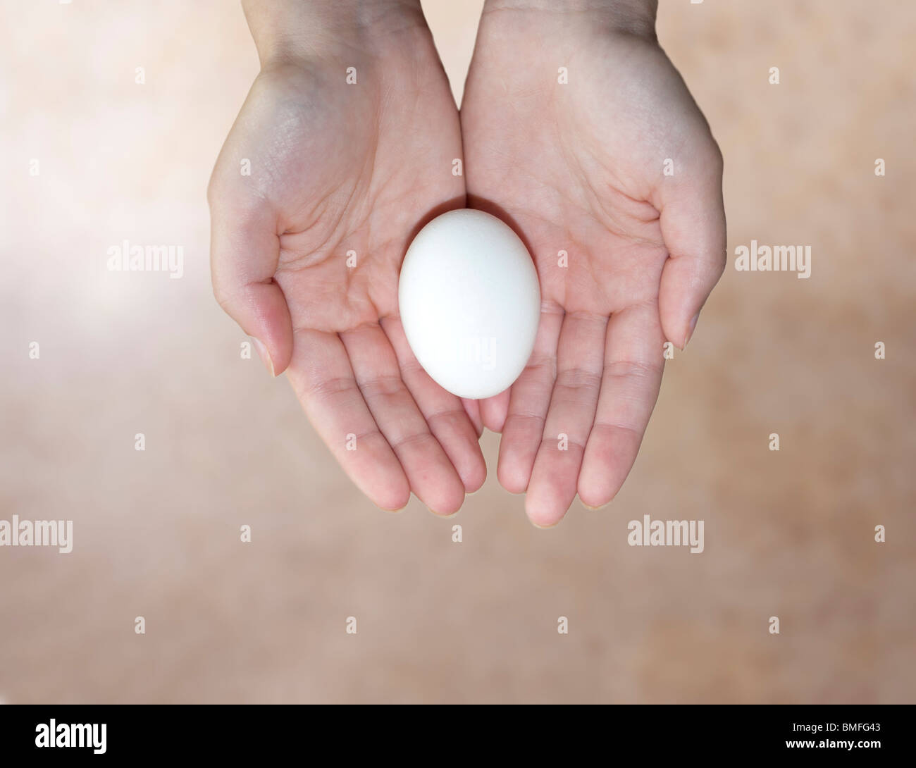 Ein Konzeptbild von einer jungen Frau Hände halten ein Ei auf einem beigen Hintergrund. Konzept der Fruchtbarkeit, Konzept-Reproduktion. Stockfoto