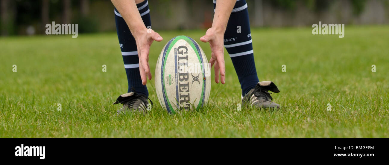 Rugby-Spieler legt einen Gilbert Rugby-Ball auf den Boden für einen Strafstoß bereit, zwei Hände sind beiderseits des Balles. Stockfoto