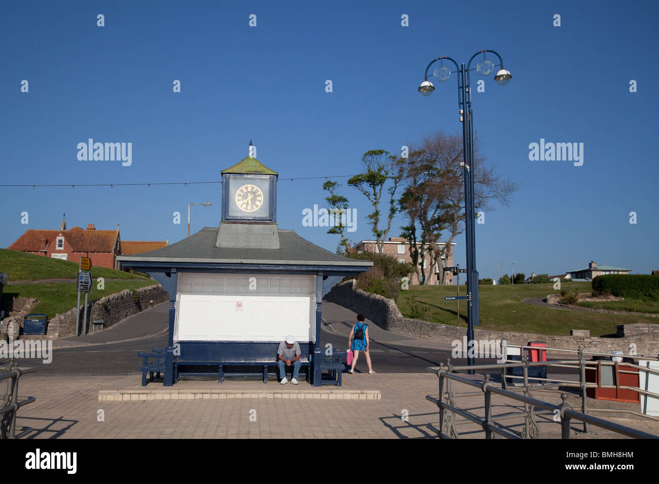 ein Mann sitzt auf Promenade Pavillion mit Uhr von der Anlegestelle / Pier im morgendlichen Sonnenlicht bei Swanage Stockfoto