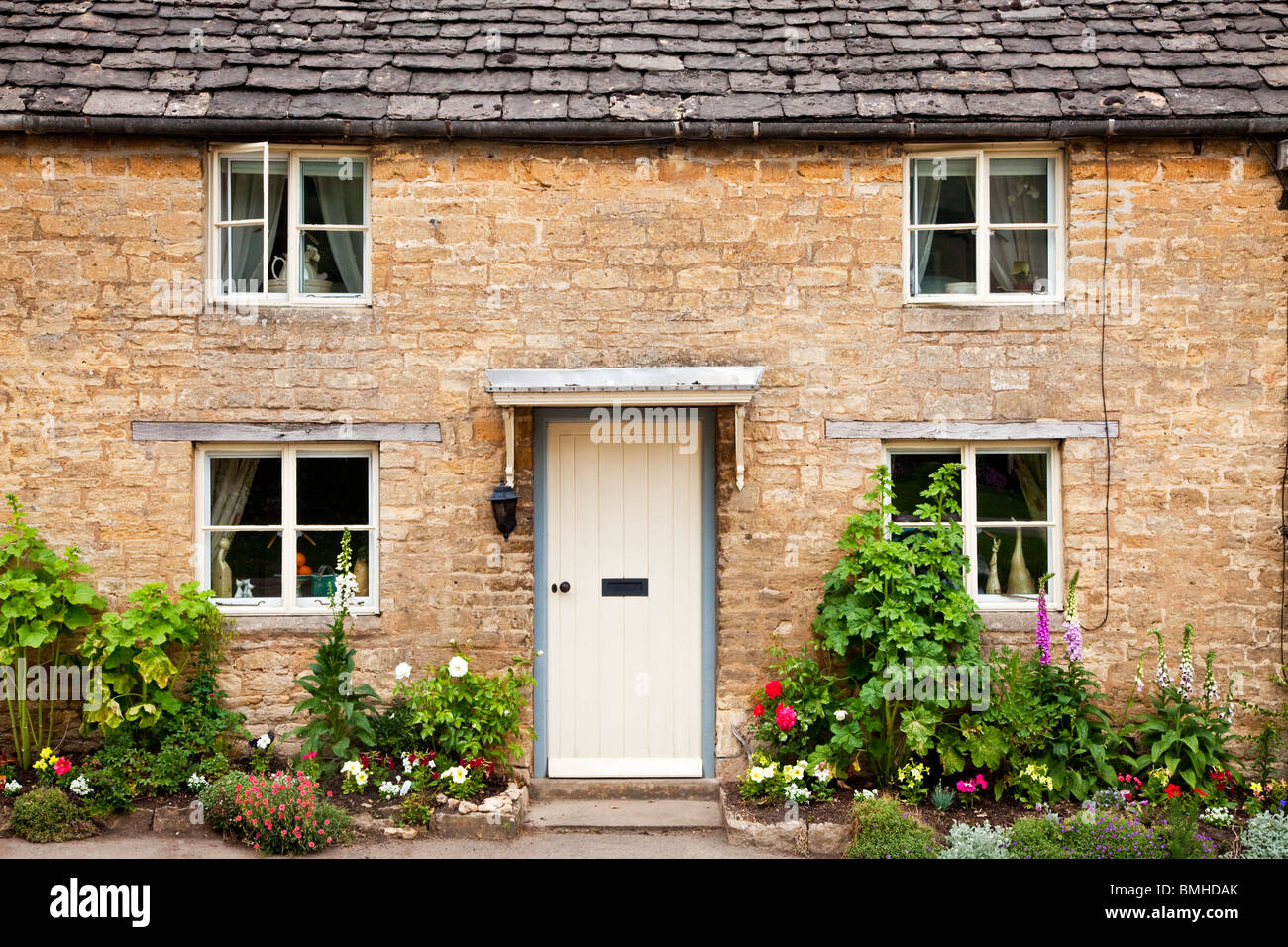 Ein typisches traditionelles Cotswold Steindorf Haus mit einem weißen hölzernen Eingangstür und hübschen Cottage-Garten Stockfoto