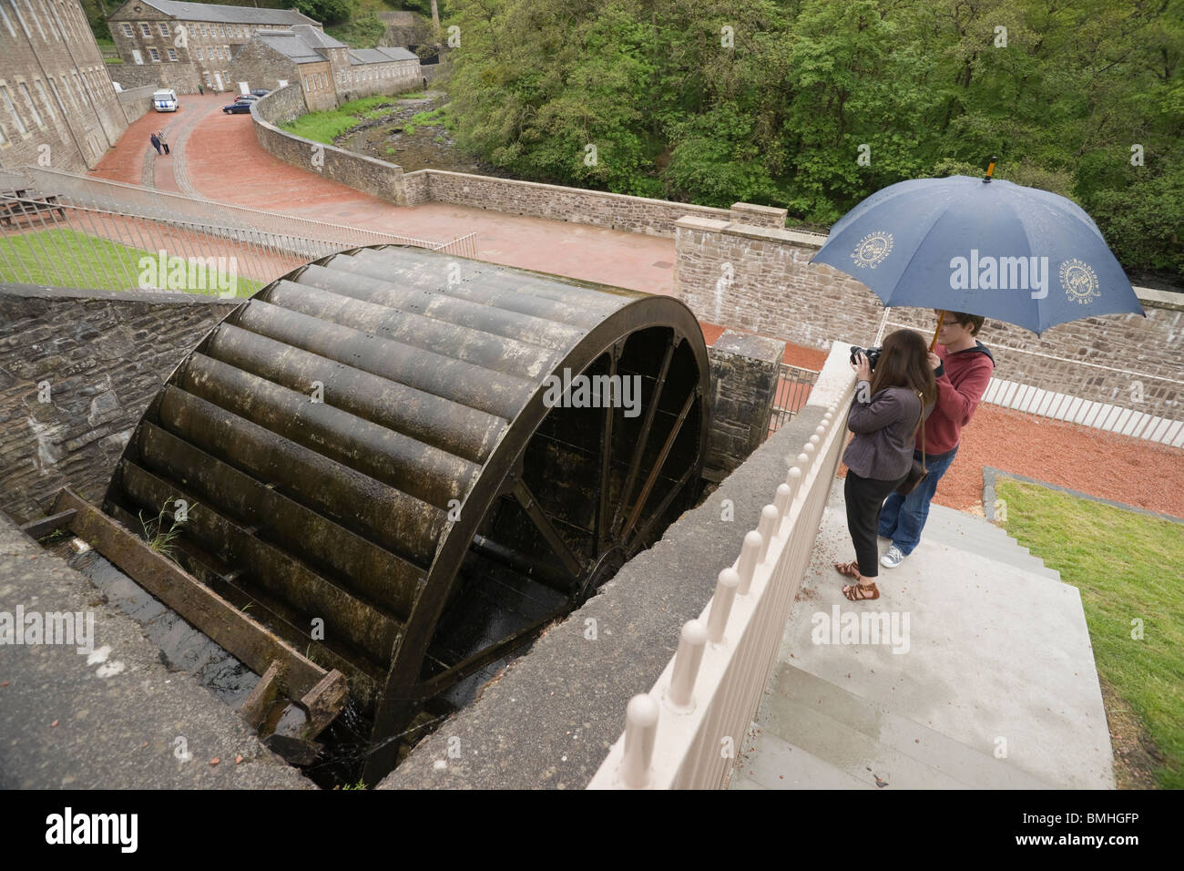 New Lanark - Robert Owen utopische Industriedorf in Schottland. Der Clyde River Wasserrad mit jungen Paar im Regen Stockfoto