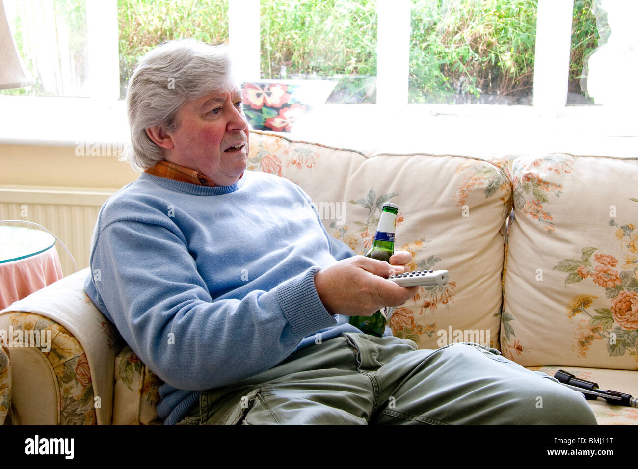 Reifer Mann halten TV remote mit Bierflasche in der hand Stockfoto