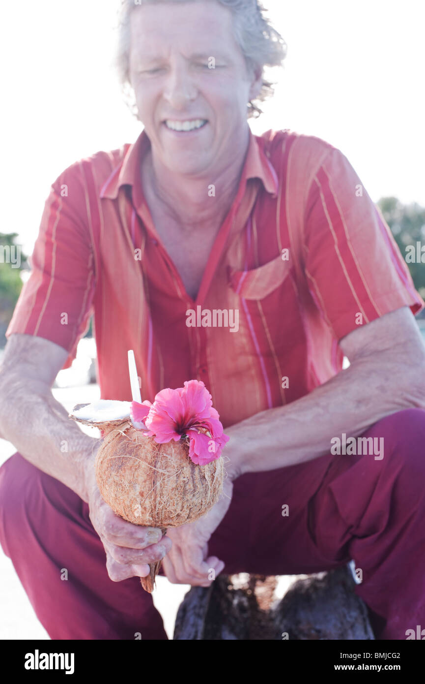 Ein Tourist auf dem Marshaller Atoll Jaluit trinkt eine frische Kokosnuss mit einer rosa Hibiskus Blume verziert. Stockfoto