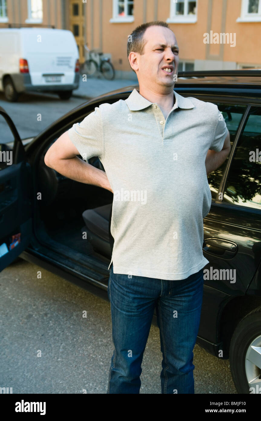Mann, der steht und sich steif neben der offenen Autotür ausdehnt. Stockfoto